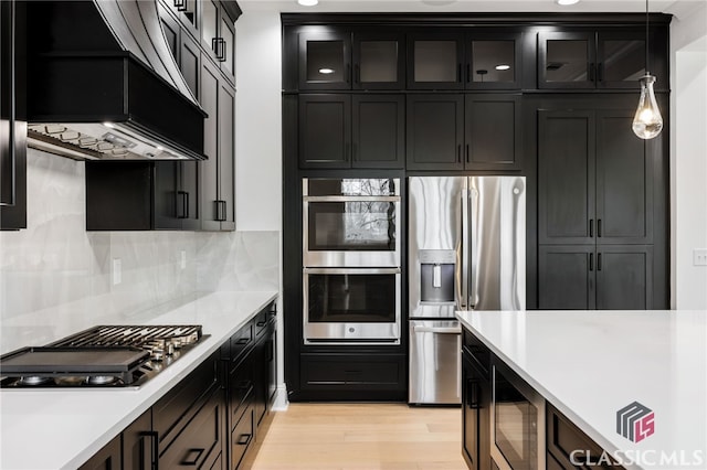 kitchen with light hardwood / wood-style flooring, stainless steel appliances, pendant lighting, backsplash, and custom exhaust hood