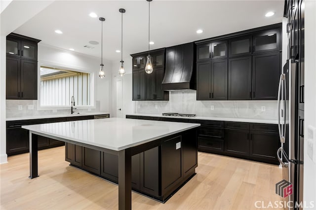 kitchen with appliances with stainless steel finishes, hanging light fixtures, premium range hood, a kitchen island, and light wood-type flooring