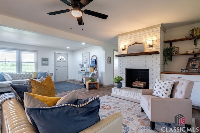 living room featuring ceiling fan, wood-type flooring, and a brick fireplace