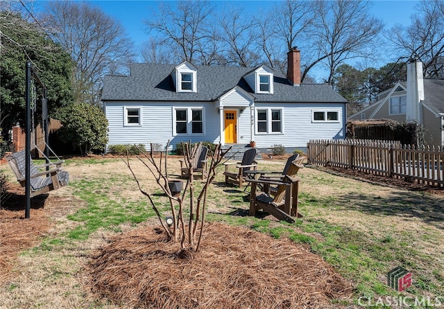 rear view of property with entry steps, fence, a yard, roof with shingles, and a chimney