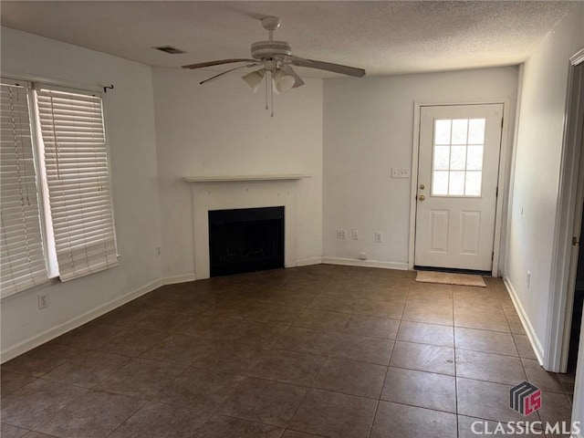 unfurnished living room with ceiling fan, dark tile patterned flooring, and a textured ceiling