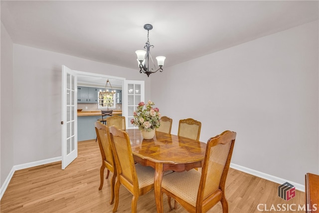 dining area featuring wood finished floors, french doors, baseboards, and an inviting chandelier