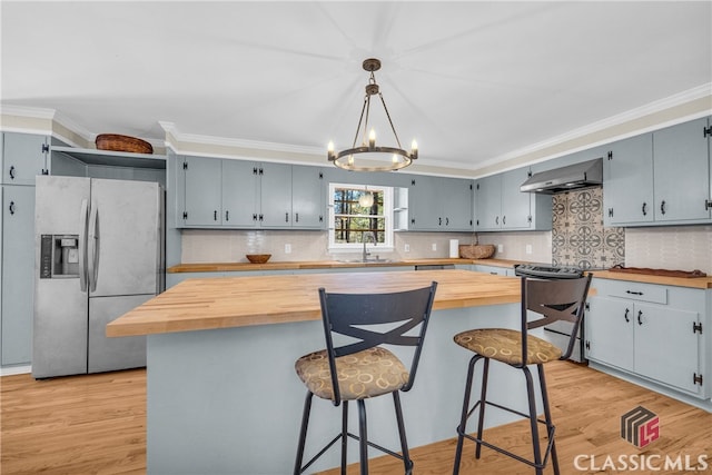 kitchen featuring a center island, a sink, stainless steel appliances, pendant lighting, and wooden counters