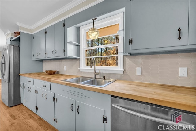 kitchen featuring stainless steel appliances, butcher block counters, a sink, ornamental molding, and pendant lighting