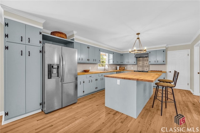 kitchen featuring a breakfast bar area, a kitchen island, wood counters, stainless steel fridge with ice dispenser, and decorative light fixtures