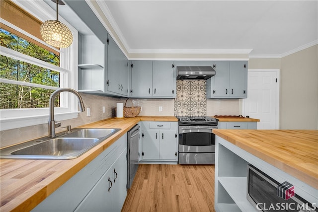 kitchen with hanging light fixtures, wall chimney range hood, wood counters, and appliances with stainless steel finishes