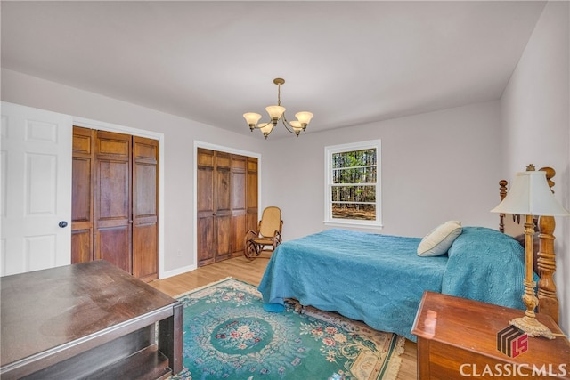 bedroom with baseboards, light wood finished floors, two closets, and an inviting chandelier