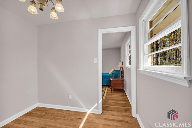 corridor featuring light wood-style floors, baseboards, and an inviting chandelier