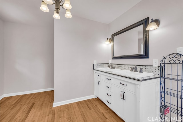 bathroom featuring double vanity, baseboards, wood finished floors, a chandelier, and a sink