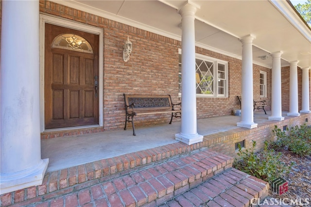 view of exterior entry featuring covered porch and brick siding