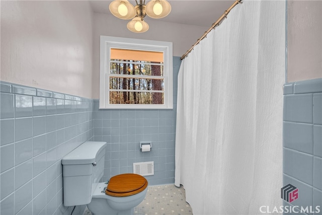 full bath featuring toilet, a wainscoted wall, visible vents, tile walls, and tile patterned floors