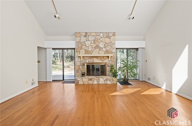 unfurnished living room featuring high vaulted ceiling, rail lighting, a stone fireplace, and wood-type flooring