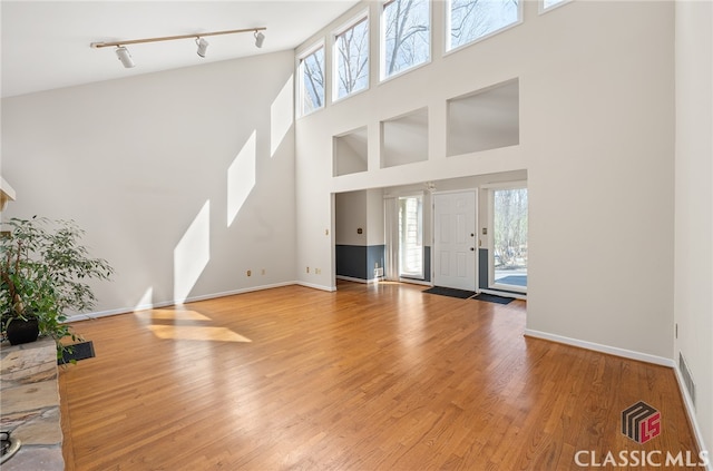 unfurnished living room with rail lighting, wood-type flooring, and a towering ceiling