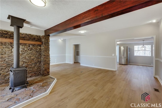 unfurnished living room with a textured ceiling, beamed ceiling, visible vents, and light wood-style floors