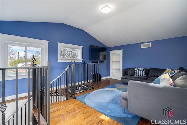 living room with lofted ceiling, built in shelves, wood finished floors, visible vents, and baseboards