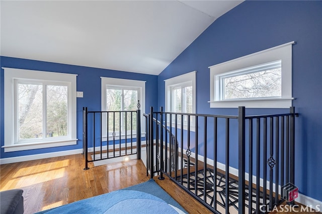 hall featuring lofted ceiling, baseboards, wood finished floors, and an upstairs landing