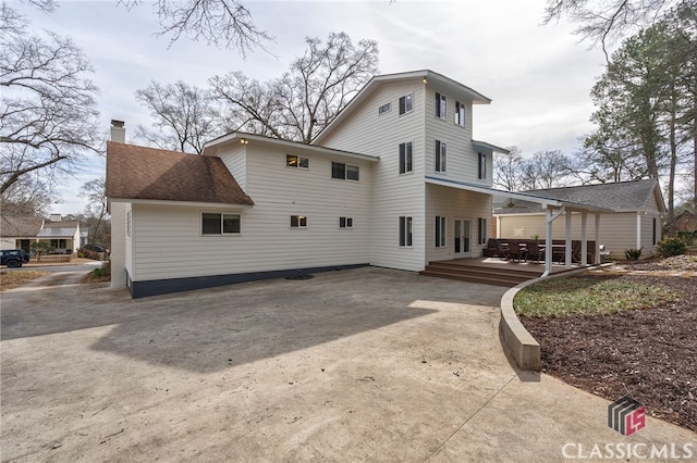 back of property featuring concrete driveway, a chimney, a patio, and roof with shingles