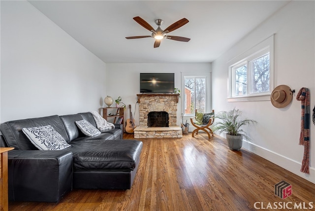 living area with ceiling fan, a stone fireplace, baseboards, and wood finished floors