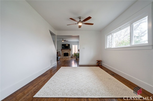 spare room featuring visible vents, baseboards, a fireplace with raised hearth, and dark wood finished floors