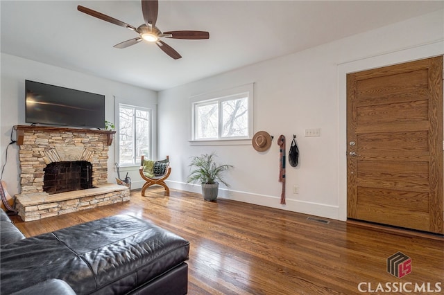 living room featuring dark wood-style floors, a fireplace, visible vents, and baseboards