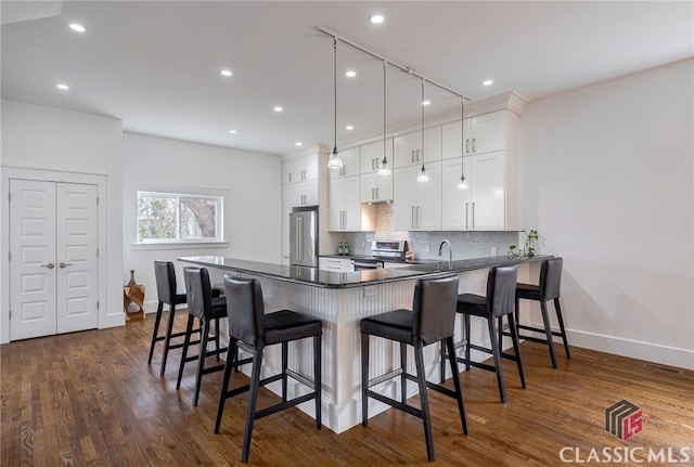 kitchen featuring a breakfast bar area, white cabinetry, appliances with stainless steel finishes, dark countertops, and pendant lighting