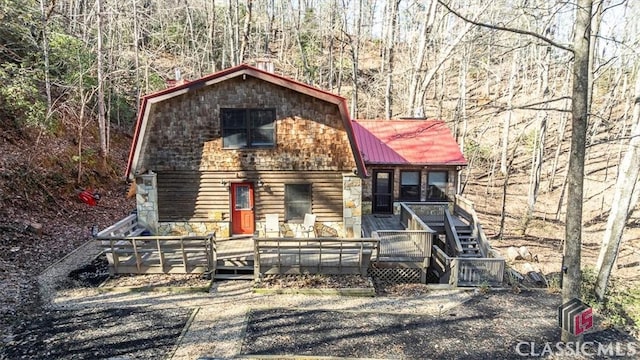 chalet / cabin with a gambrel roof, metal roof, a deck, a forest view, and stairs