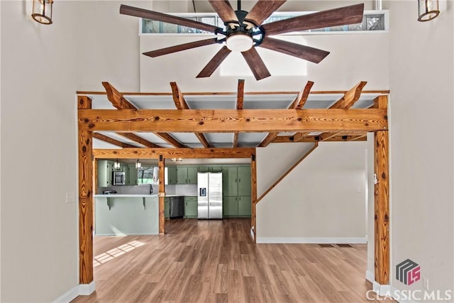 interior space with a ceiling fan, wood finished floors, beam ceiling, and baseboards