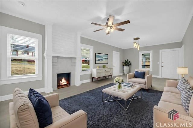 living area with a warm lit fireplace, ceiling fan, and baseboards