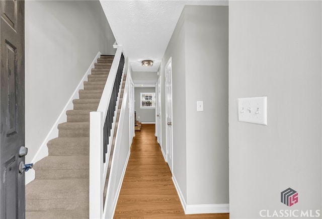 foyer entrance featuring stairs, a textured ceiling, wood finished floors, and baseboards