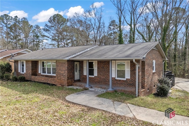 ranch-style home with a shingled roof, a front yard, covered porch, and brick siding