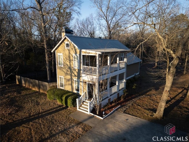 view of front of home with a chimney, metal roof, a balcony, and fence