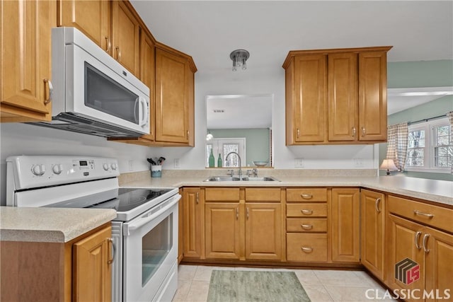 kitchen featuring light tile patterned floors, light countertops, brown cabinetry, a sink, and white appliances