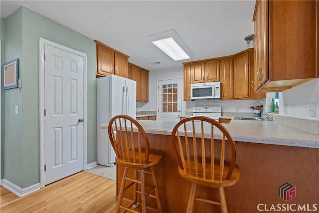 kitchen featuring white appliances, brown cabinetry, light countertops, light wood-style floors, and a sink