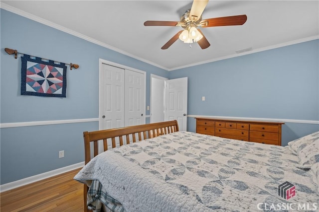 bedroom featuring wood finished floors, a ceiling fan, baseboards, a closet, and crown molding