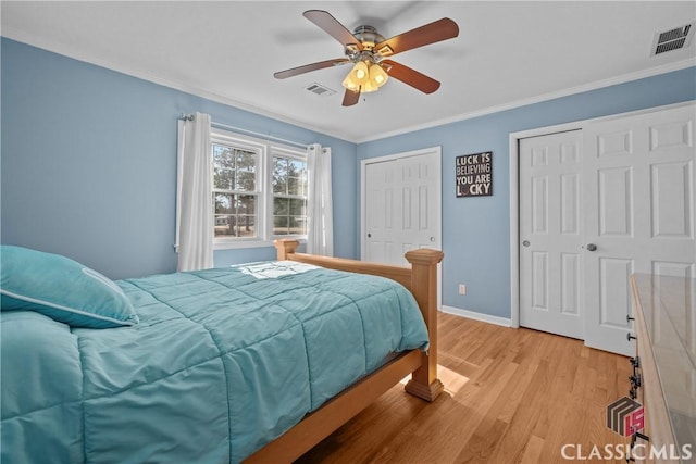 bedroom with light wood-style floors, crown molding, visible vents, and two closets