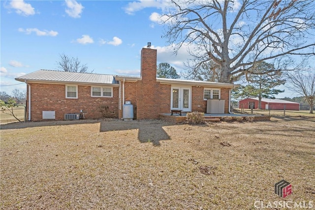 back of house featuring french doors, brick siding, a chimney, central air condition unit, and metal roof