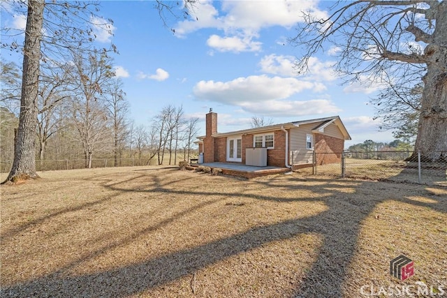 view of front of home featuring brick siding, a patio, a chimney, a fenced backyard, and a front lawn