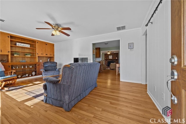 living room with built in shelves, light wood finished floors, visible vents, ornamental molding, and ceiling fan