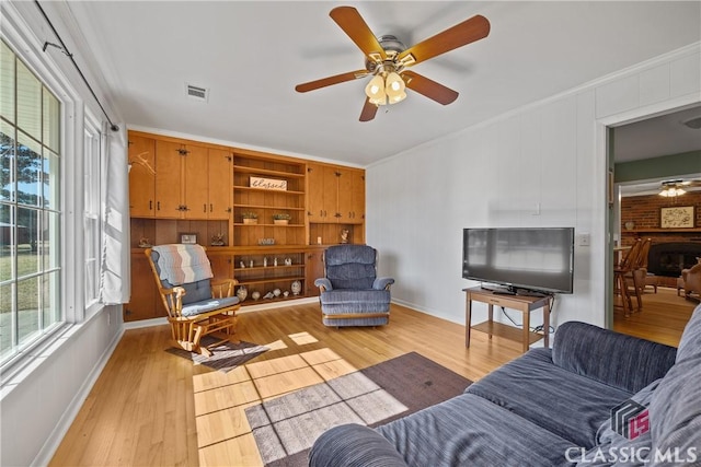 living area with light wood-style floors, visible vents, ornamental molding, and ceiling fan