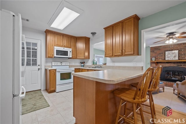 kitchen featuring a breakfast bar area, light countertops, brown cabinetry, white appliances, and a peninsula