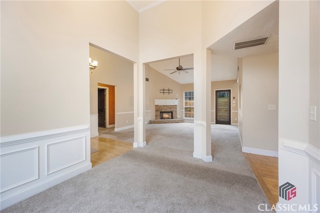 empty room with light colored carpet, visible vents, wainscoting, ceiling fan, and a stone fireplace