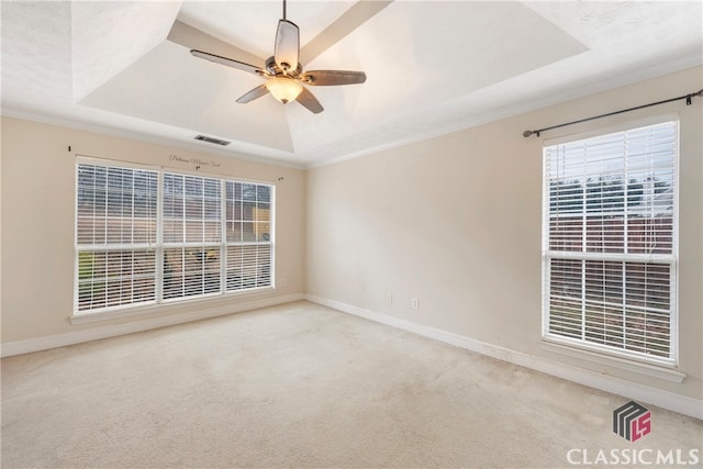 empty room featuring a tray ceiling, visible vents, and light colored carpet