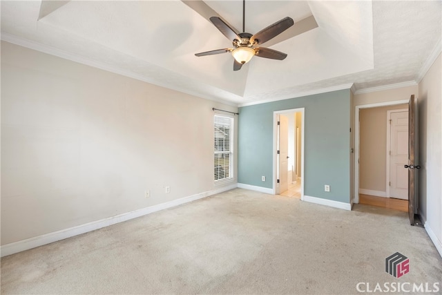 unfurnished bedroom with light colored carpet, baseboards, ornamental molding, a tray ceiling, and ensuite bath