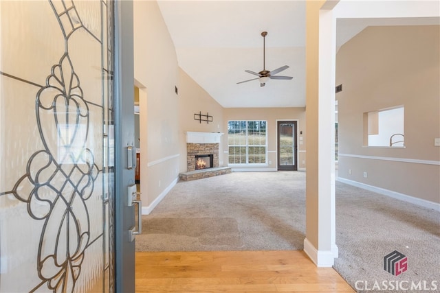 foyer entrance featuring ceiling fan, high vaulted ceiling, a stone fireplace, and carpet flooring