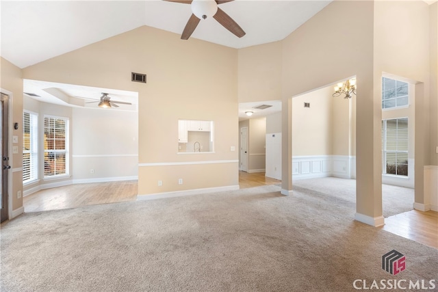 interior space featuring high vaulted ceiling, light colored carpet, visible vents, and ceiling fan with notable chandelier