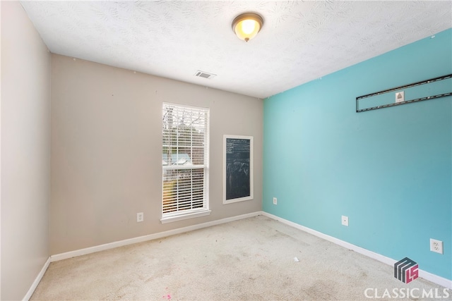 spare room with a textured ceiling, baseboards, visible vents, and light colored carpet