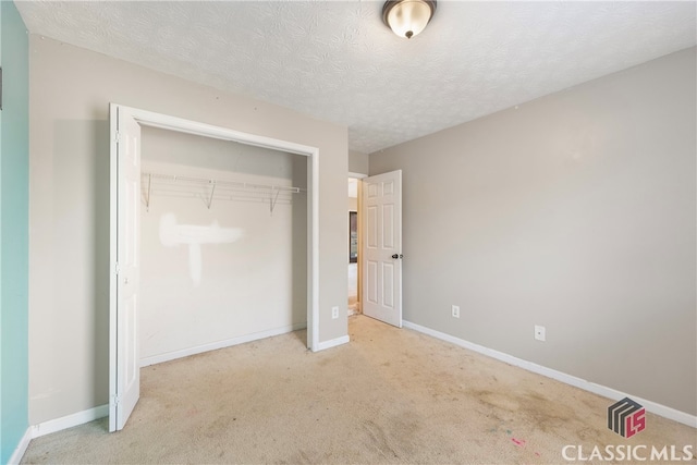 unfurnished bedroom with a textured ceiling, a closet, light colored carpet, and baseboards