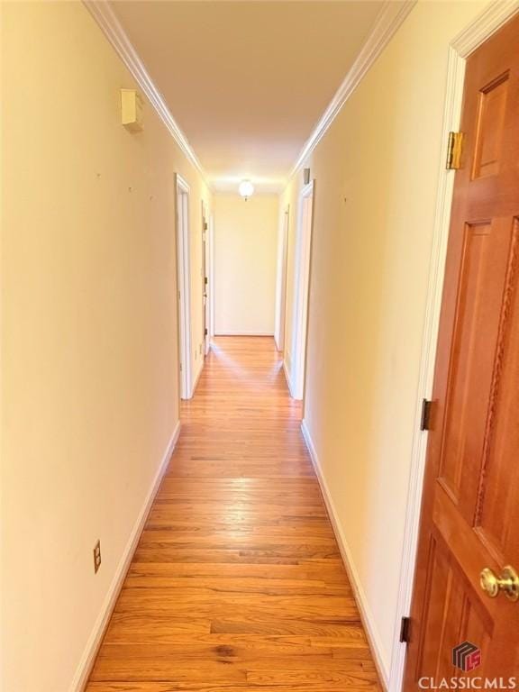 hallway with light wood-style flooring, baseboards, and crown molding