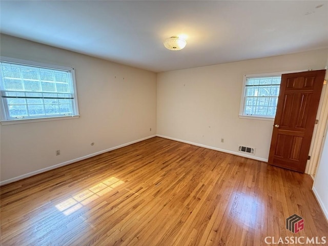 empty room featuring a wealth of natural light, baseboards, visible vents, and light wood finished floors