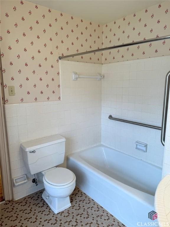 bathroom featuring tile walls, wallpapered walls, toilet, tile patterned flooring, and wainscoting